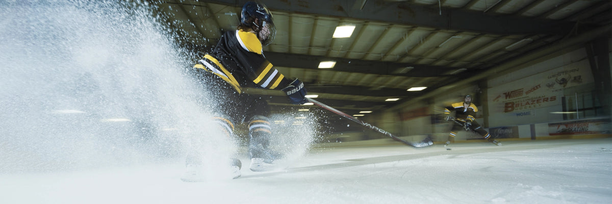 Two people playing hockey on an indoor ice rink. 