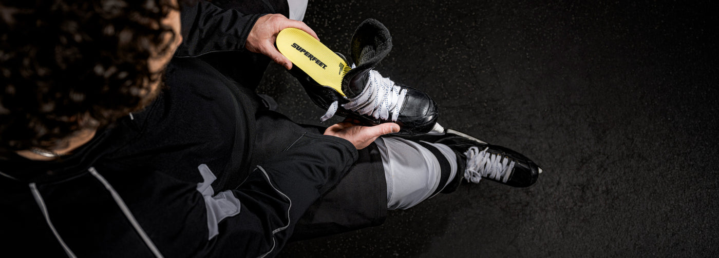 Person putting on a black and white hockey skate with  Superfeet skate insole on a dark background. 