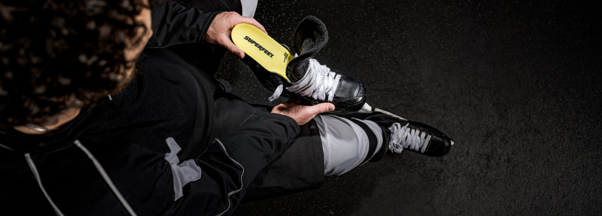 Person putting on a black and white hockey skate with  Superfeet skate insole on a dark background. 