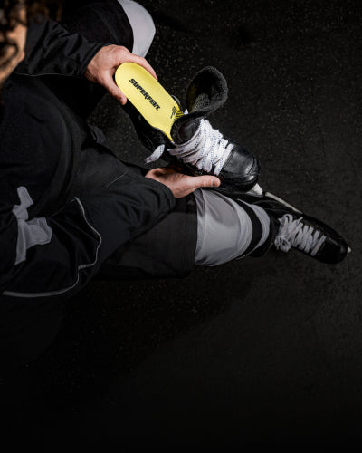 Person putting on a black and white hockey skate with  Superfeet skate insole on a dark background. 