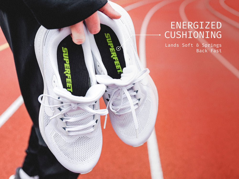 Someone standing on a track holding Superfeet's Run Pacer Insole inside of a white running shoe. Text Reads "Energized Cushioning Land Soft & Springs Back Fast" 