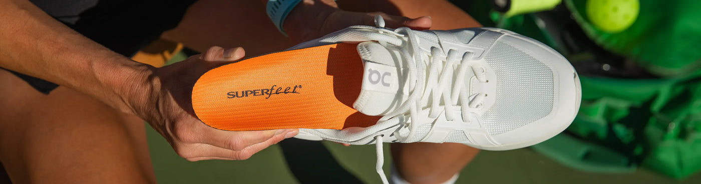 Man holding shoe and inserting a Superfeet All Purpose High Impact Support Orange insole into shoe.